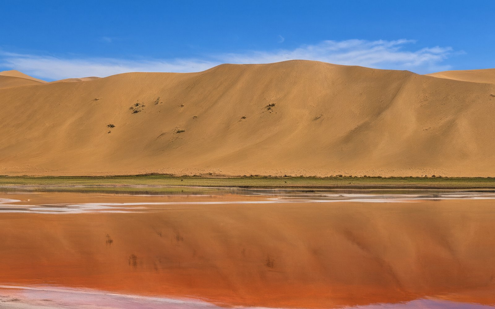 High golden dune above orange-red water at Badain Lake