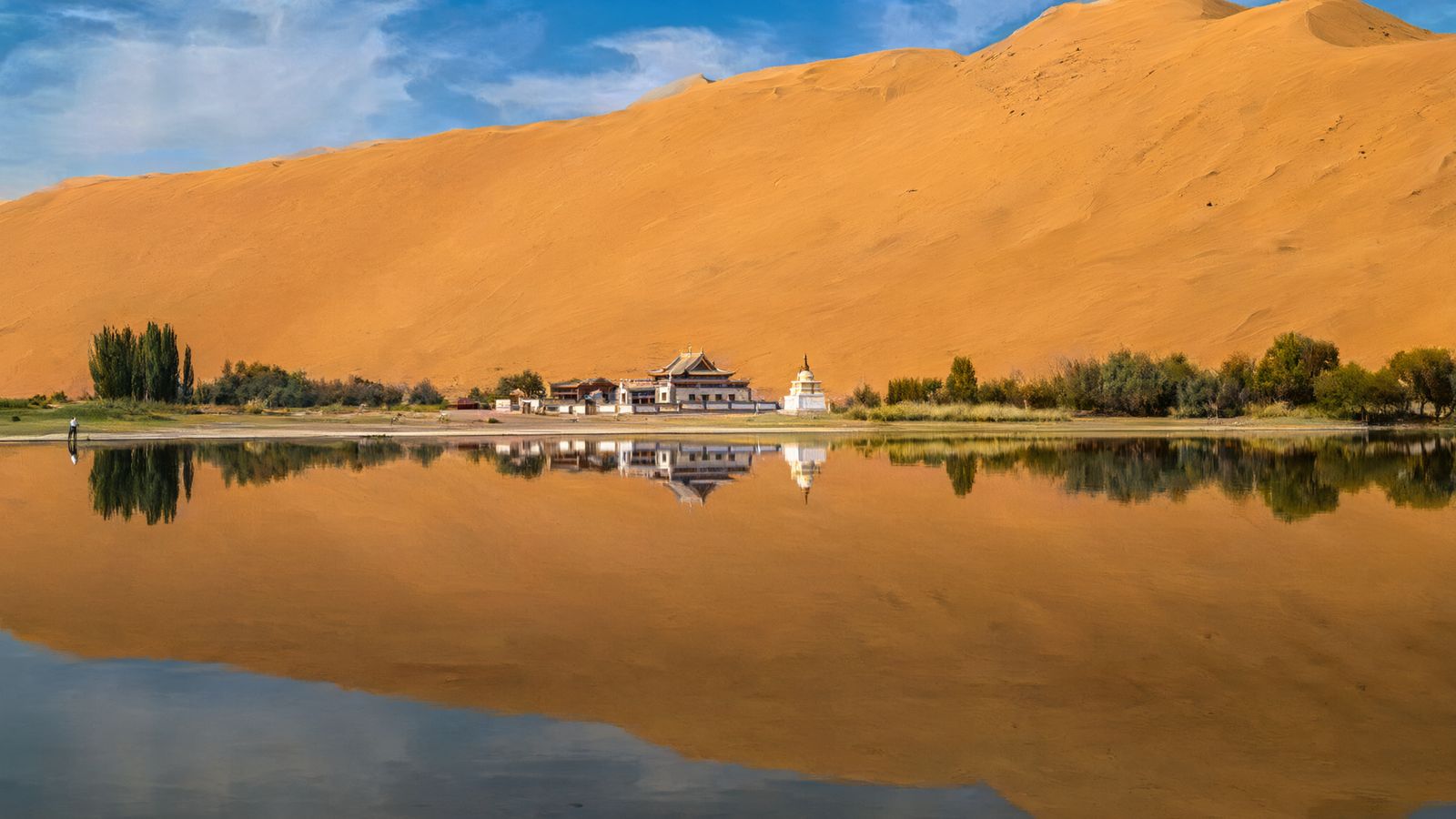 White temple buildings on the shore of Miao Haizi with a high dune behind
