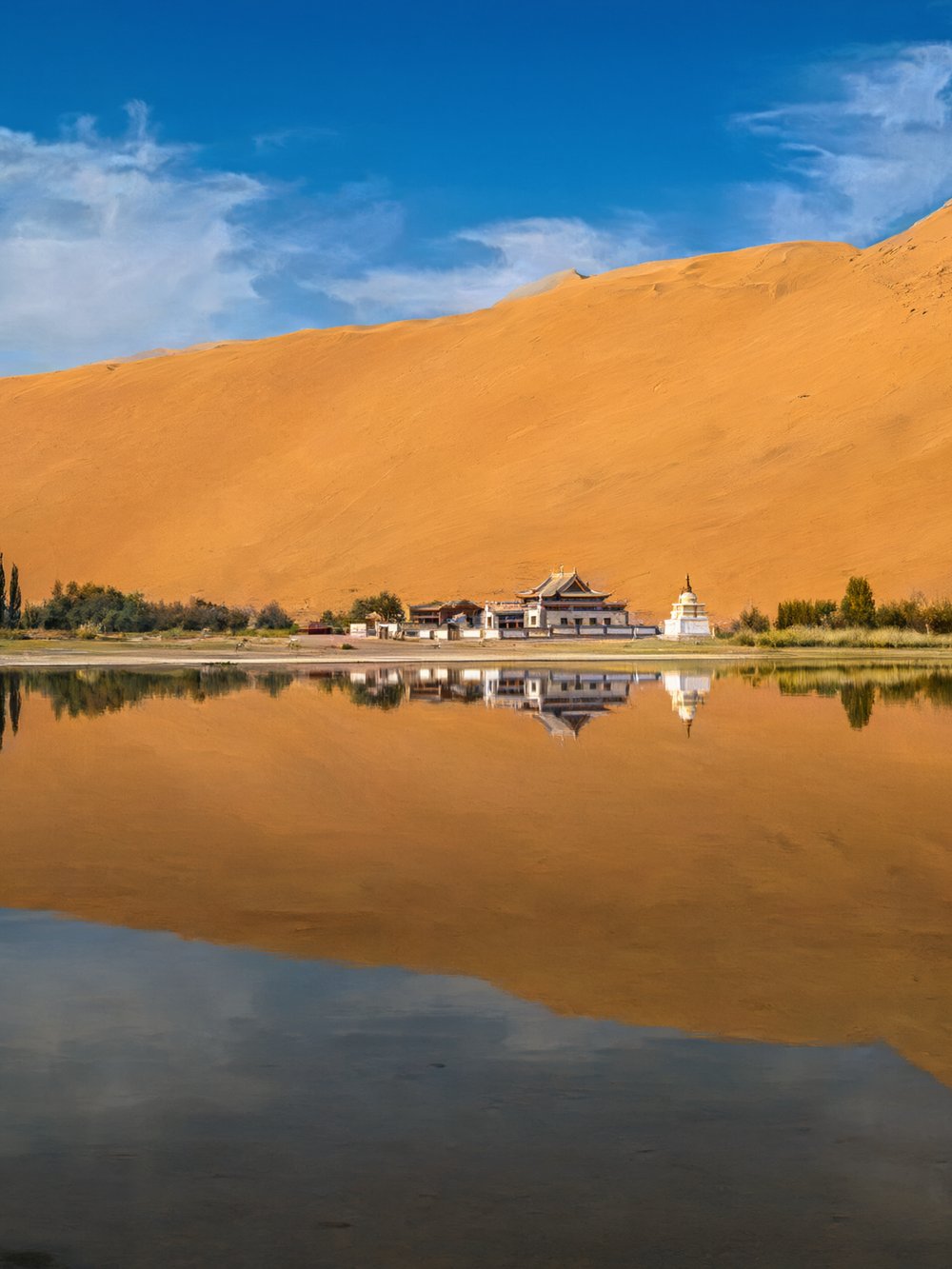 White temple buildings on the shore of Miao Haizi with a high dune behind