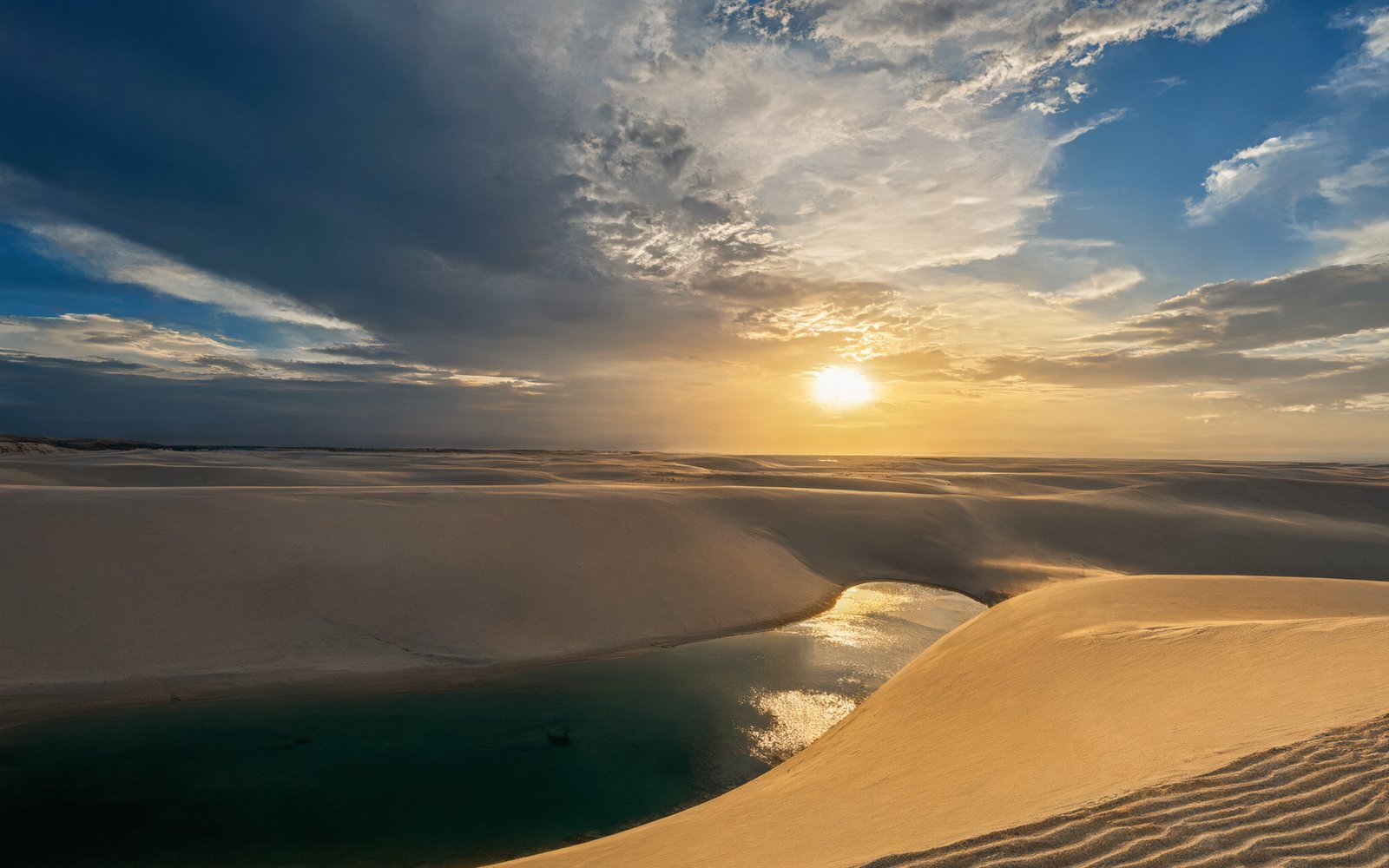 Low sun over sand ridges and a dark pool of water at Nuoertu Lake