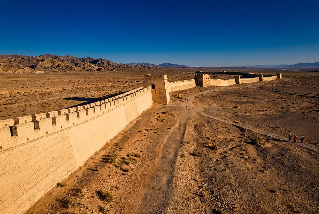 Jiayuguan Great Wall running across the Gobi desert plain toward the horizon beacon towers rammed earth late afternoon light Gansu