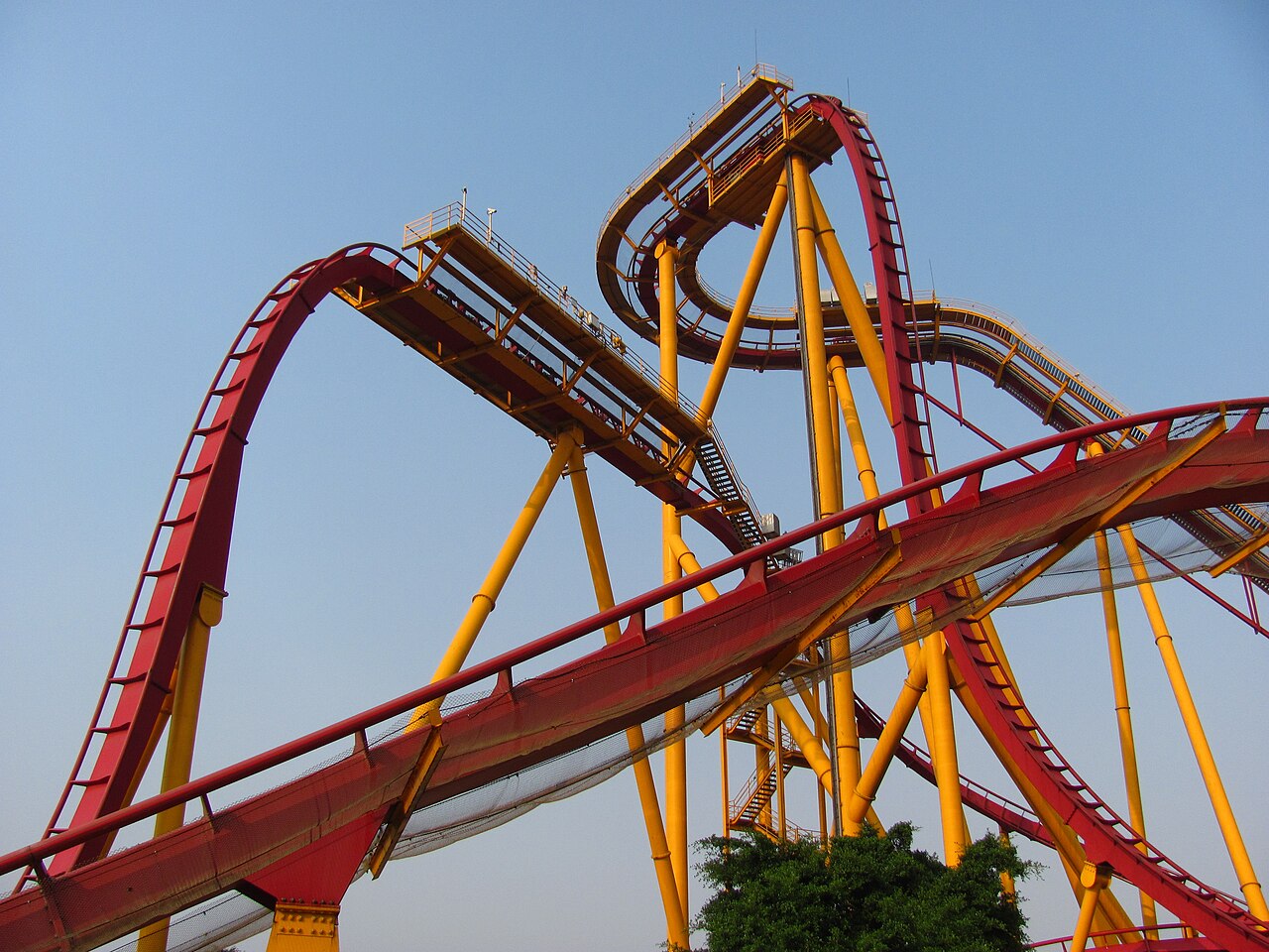 Looping red and yellow roller coaster tracks crossing against a blue sky