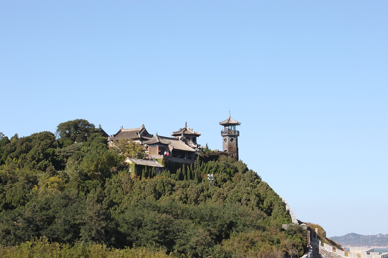 A tower and temple roofs on top of a wooded hill under a clear blue sky