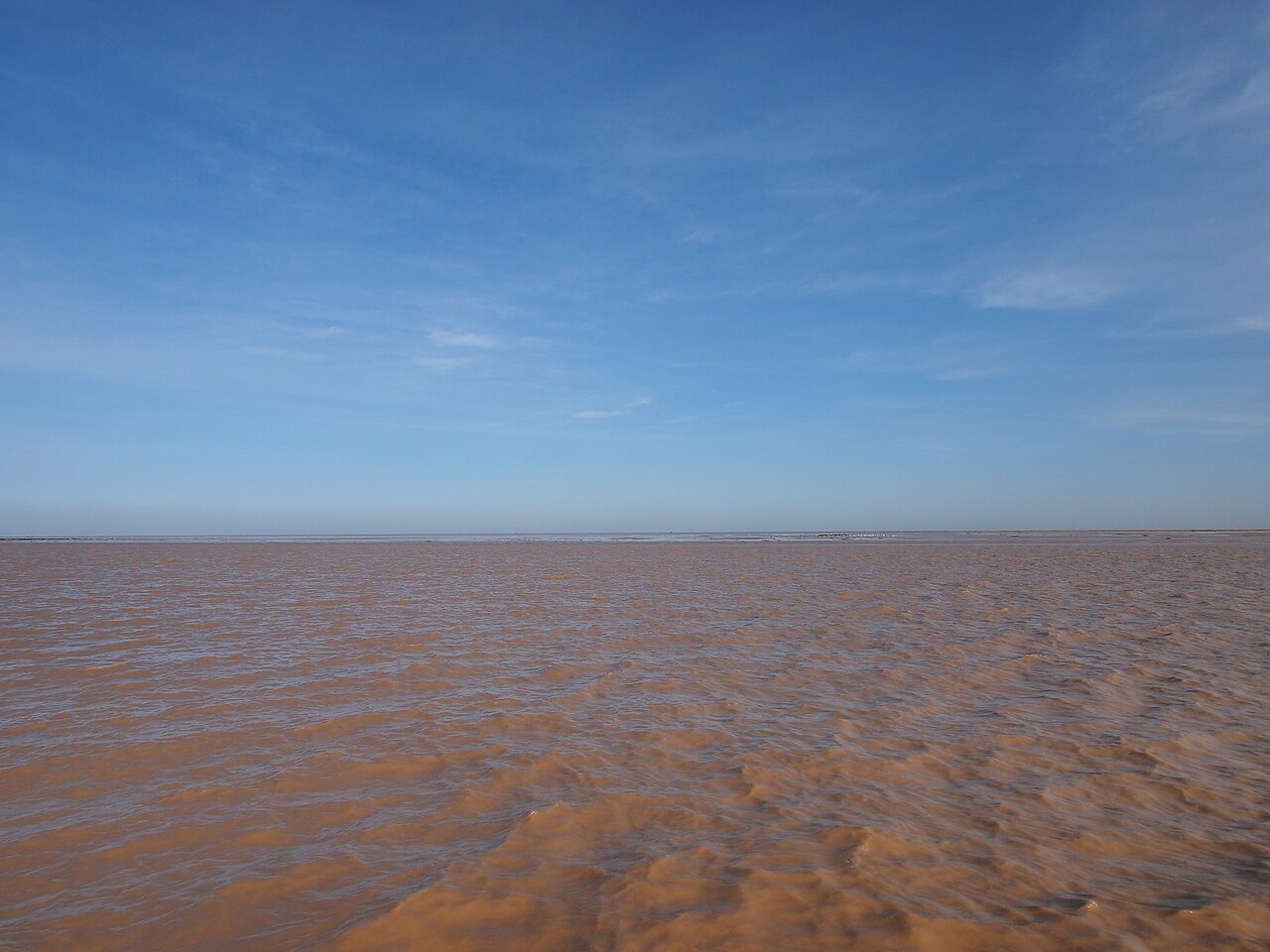 A broad flat stretch of brown rippled water out to a level horizon under a deep blue sky