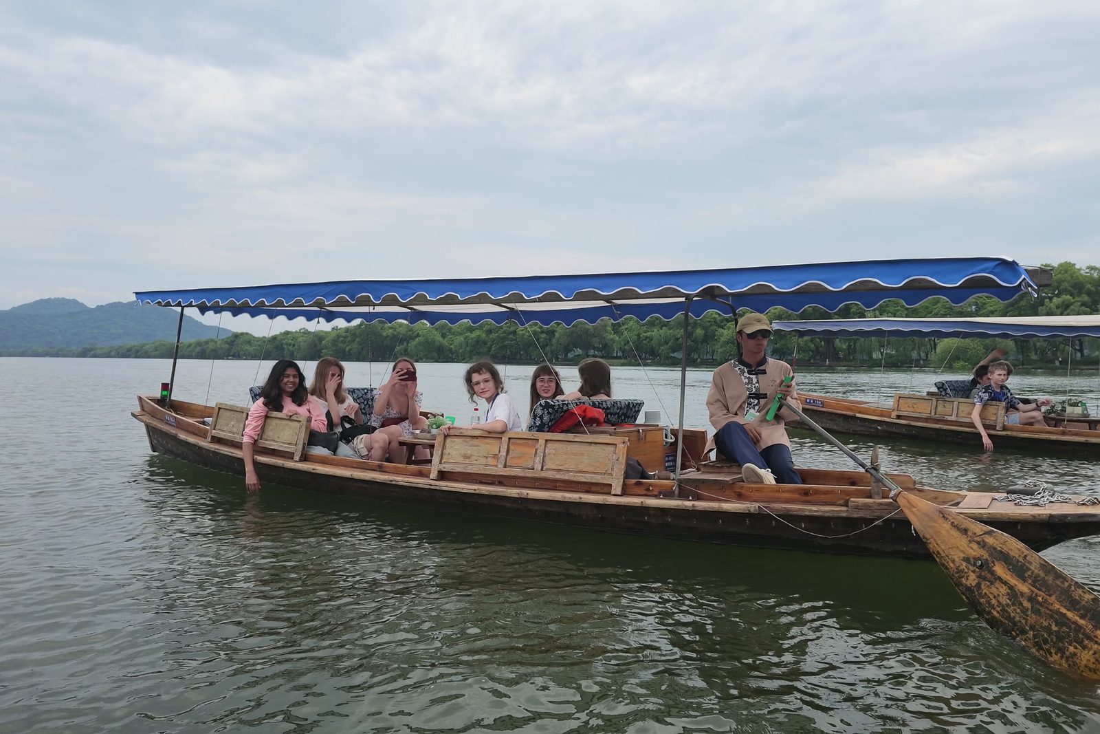 A wooden tourist boat with a blue canopy crossing West Lake in Hangzhou